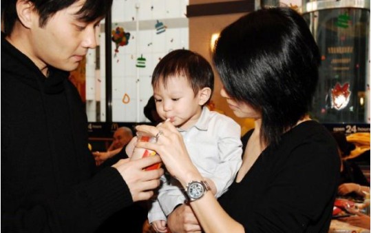 袁咏仪晒出早年家庭合影：袁咏仪抱着儿子给他喂饮料喝，三人表情呆萌